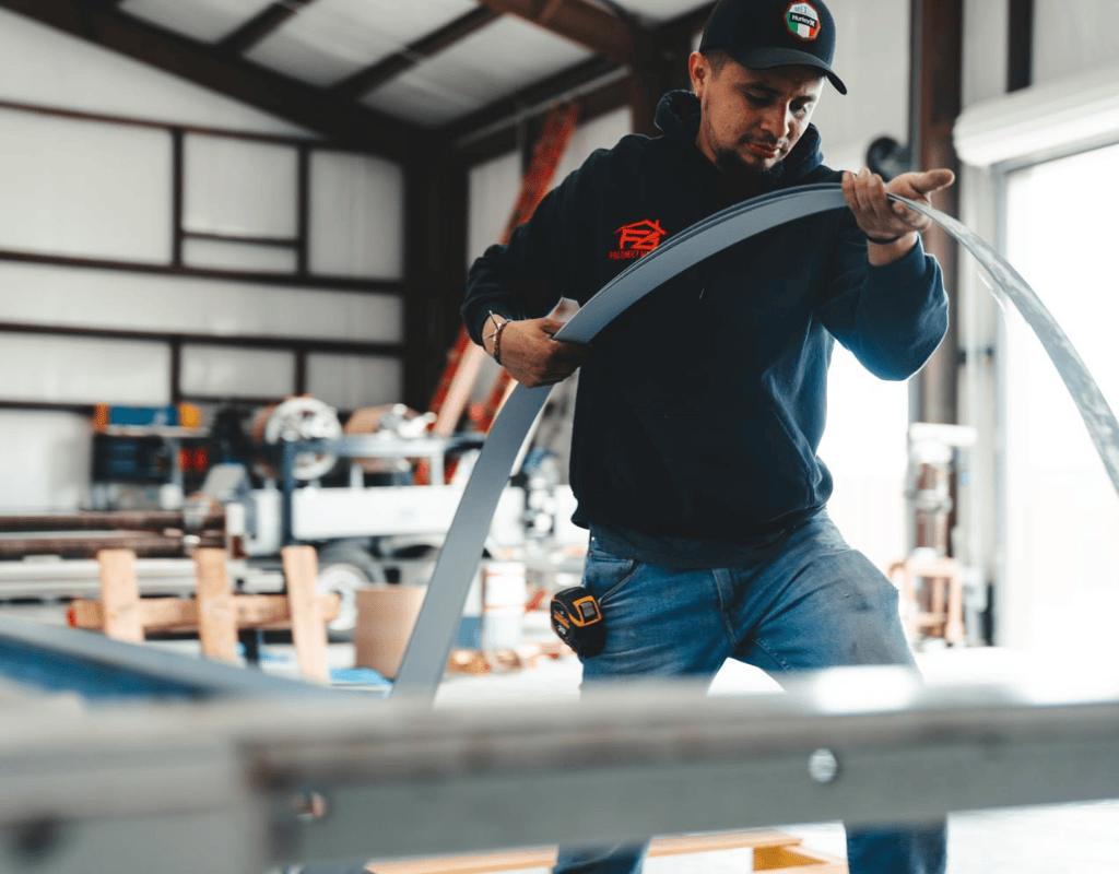 Technician inspecting and guiding a curved sheet through a custom break-metal machine at AM Sheet Metal and Roofing Supply in Central Texas.