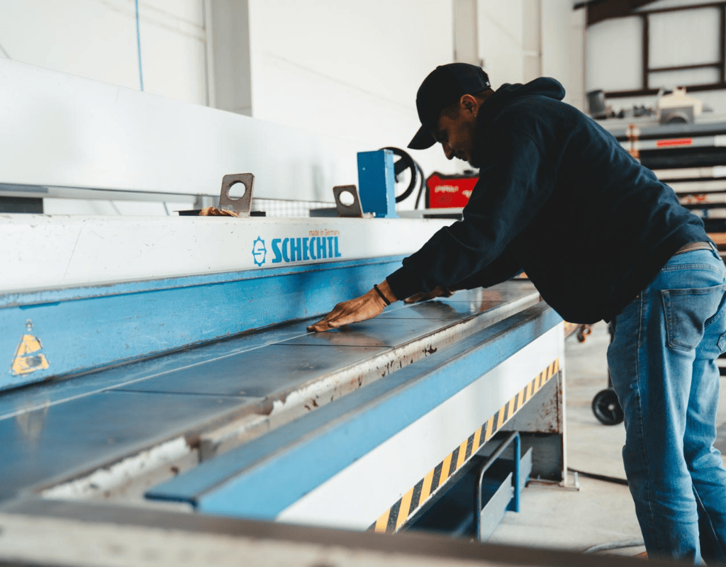 Worker feeding a flat sheet into a Schechtl brake for precise custom break-metal bending at AM Sheet Metal and Roofing Supply.
