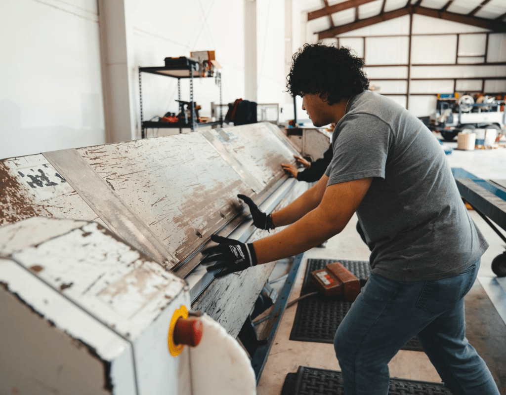 Crew member carefully bending metal flashing and trim on a sheet-metal brake inside AM Sheet Metal’s Central Texas shop.