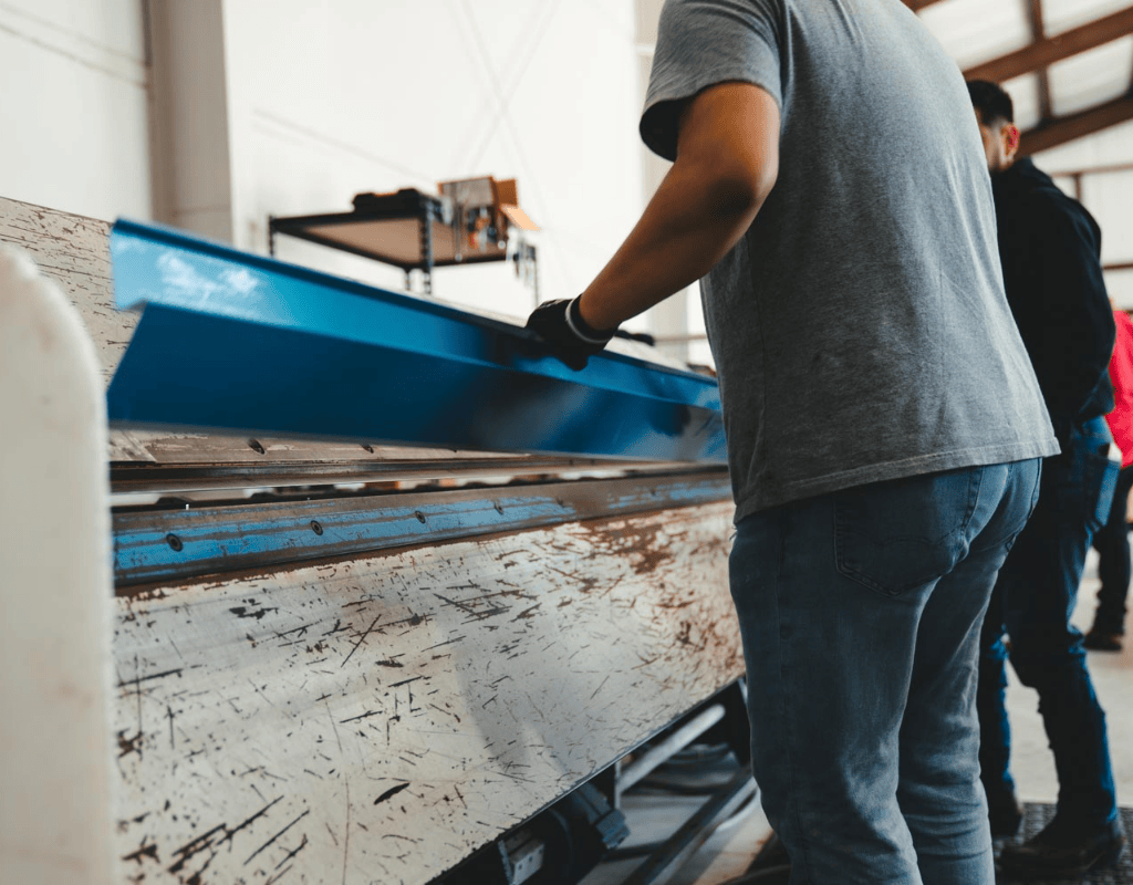 Close-up of technician feeding a painted panel into a metal brake to form flashing trim at AM Sheet Metal and Roofing Supply.